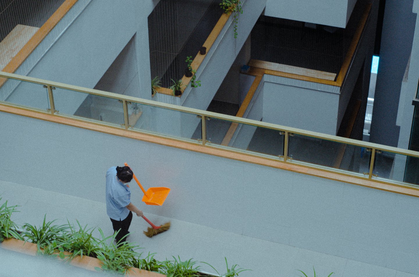 Facilitymitarbeiter fegt modernes Bürointerieur mit orangefarbenem Besen.
